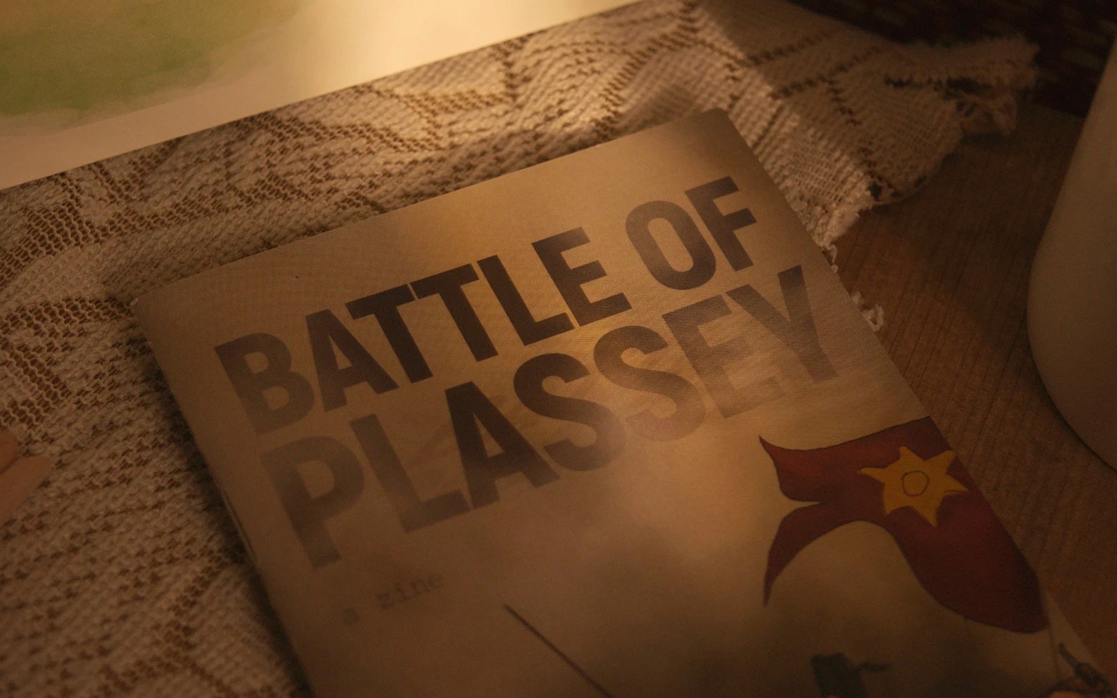 Close-up of the Battle of Plassey zine cover with its red flag emblem on lace