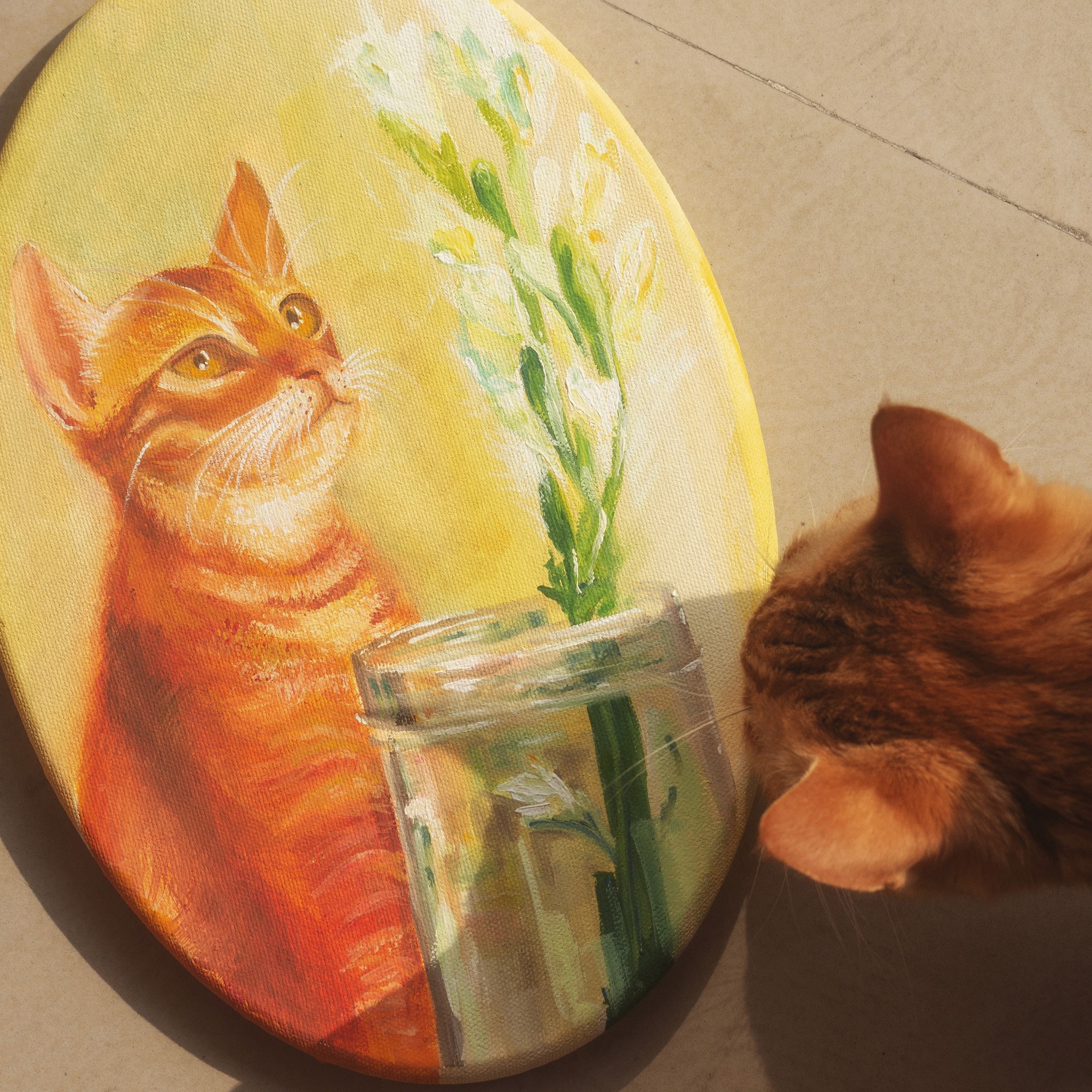 Oil painting on an oval canvas of an orange tabby cat beside a glass jar of tuberose stems, with a real cat peeking in