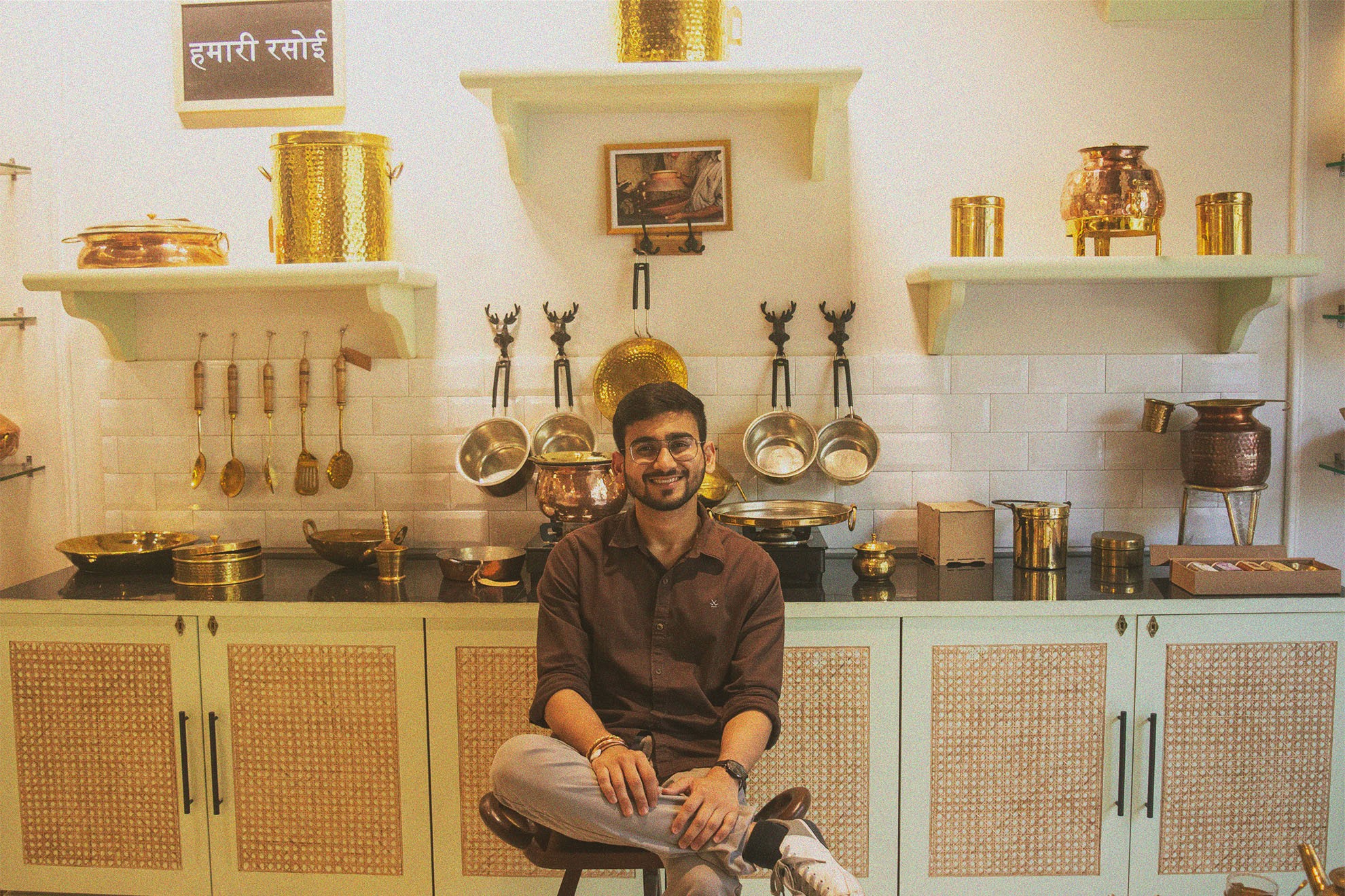 Snapshot of P-Tal founder Aditya Agrawal smiling in a kitchen full of traditional Indian brassware